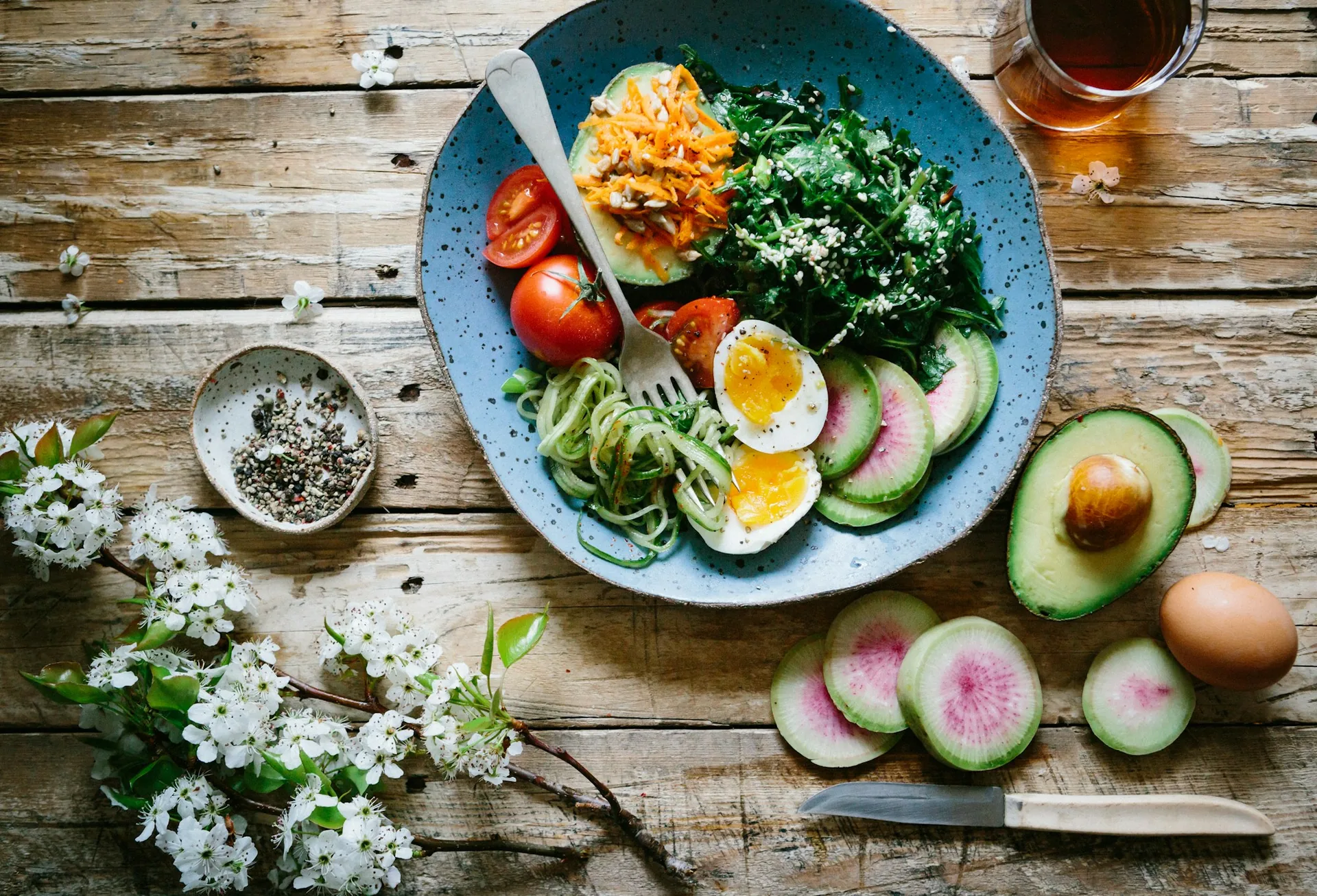 A bowl of salad with tomato, avocado, radish and a boiled egg on a wooden table
